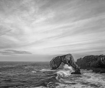 grayscale photo of seashore with rock formations thumbnail