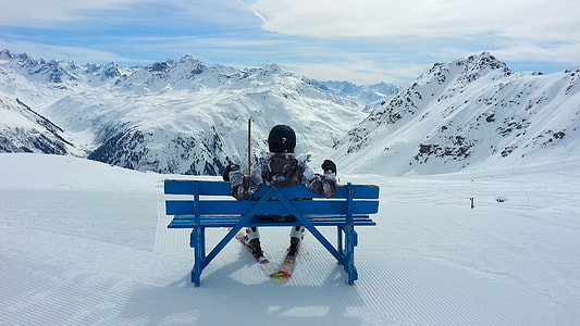 person sitting on blue wooden bench on ice coated place in front of mountains at daytime thumbnail