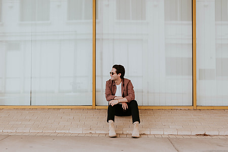 man in brown suit jacket with pants and brown boots outfit sitting beside clear glass framed window thumbnail