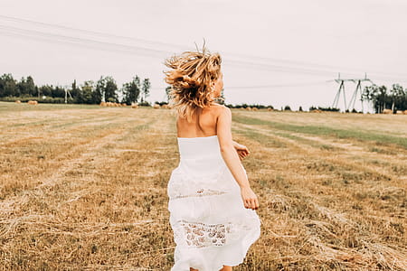 Woman Wearing White Off-shoulder Long Dress While Running on Brown Grass Field thumbnail