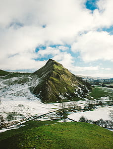 landmark photography of mountain and open field covered with snow under white and blue cloudy skies thumbnail