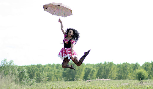 woman holding brown umbrella jump in the air with green trees as background thumbnail