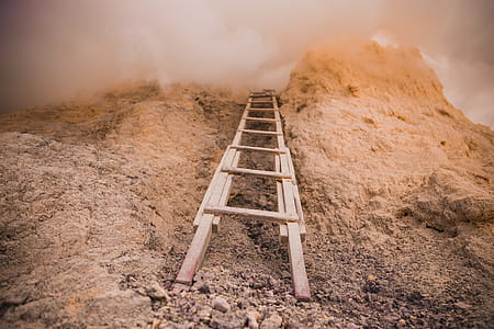 A wooden ladder placed against a rock covered with clouds on an overcast day thumbnail
