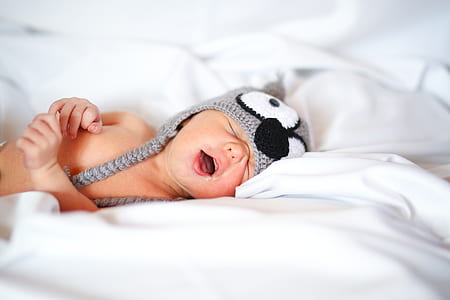 baby wearing black and white knitted owl critter hat lying on white textile thumbnail