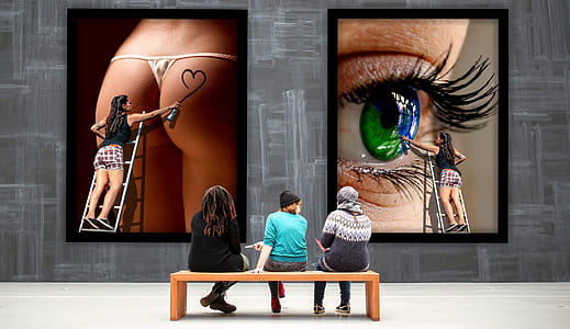 three people sitting on wooden bench in front of two artworks thumbnail