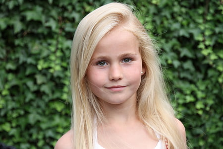smiling girl wearing white halter shirt standing near green leaf plants thumbnail