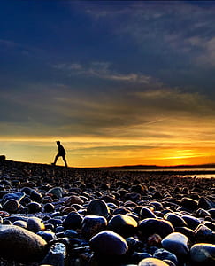 silhouette of person walking near stones and body of water during golden hour thumbnail