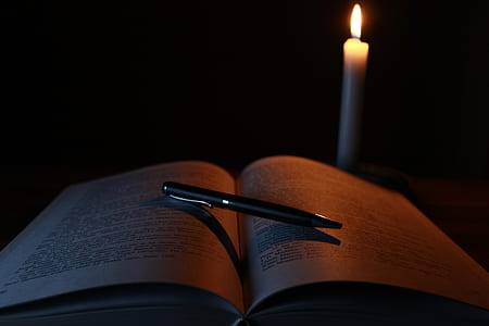 black click pen on open book near cnadle thumbnail