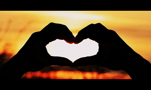 silhouette of hand forming heart during sunset thumbnail