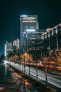 time-lapse photography of vehicle passing through the road near buildings and trees during night time thumbnail