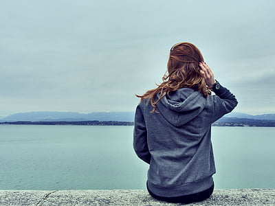 woman wearing gray hoodie overlooking body of water thumbnail