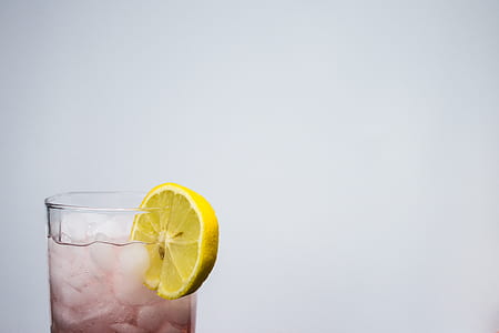 clear drinking glass filled with brown liquid, ice cubes, and sliced lemon thumbnail