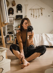focus photo of woman in brown sweater and black bottoms holding black DSLR camera thumbnail