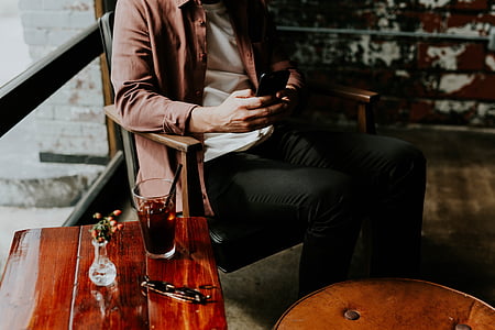 man holding black smartphone sitting on brown wooden armchair thumbnail