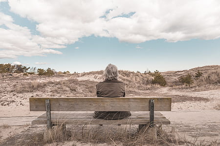 man wearing grey vest sitting on bench under white cloudy sky during daytime thumbnail