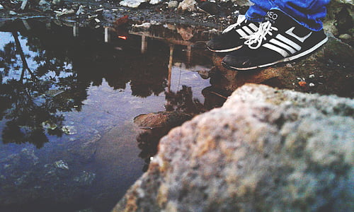 person in black sneakers standing by body of water thumbnail