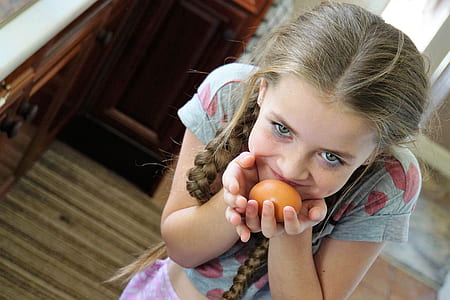 girl holding brown egg near cupboard thumbnail