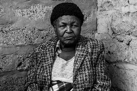 grayscale photo of woman wearing coat sitting beside concrete wall thumbnail