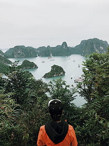 man wearing cap standing beside trees near body of water thumbnail