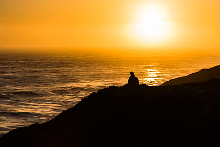 silhouette of person on cliff near body of water during sunset thumbnail