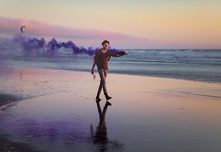 man walking on seashore while holding smoke machine thumbnail