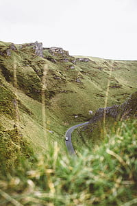 gray car cruising on asphalt road through green mountain thumbnail