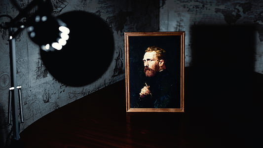 man wearing black coat painting with brown wooden frame near turned-on lamp thumbnail