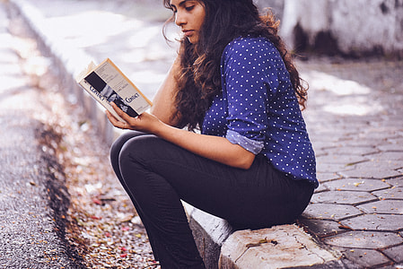 woman sits on sidewalk reading book thumbnail