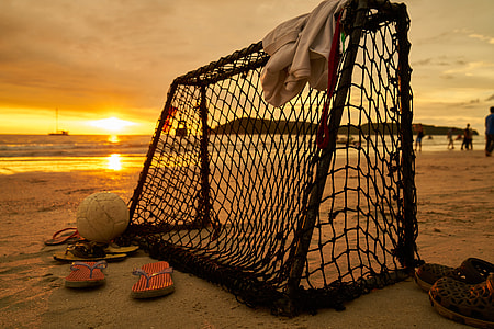silhouette photography of goal net beside flip-flops on sand at golden hour thumbnail