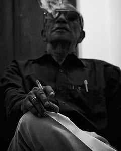 grayscale photography of man sitting on chair while smoking cigarette thumbnail