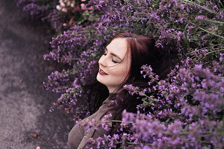 smiling woman beside purple petaled flowers thumbnail