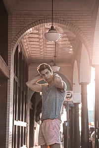 man standing below pendant lamp beside concrete wall thumbnail