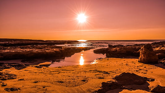 silhouette photography of rock near body of water at golden hour thumbnail
