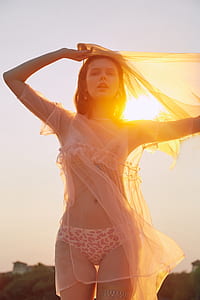 woman wearing bikini and cover ups holding see-through scarf standing near hill during daytime thumbnail