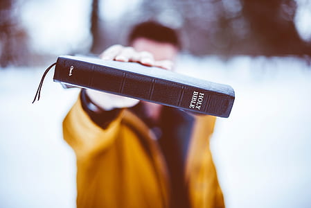 selective focus photography of man wearing brown jacket holding brown Holy Bible thumbnail