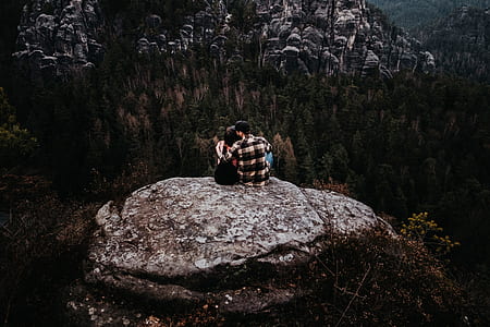 couple sitting on rack overlooking of trees near rock formation thumbnail