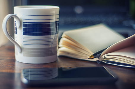 white and blue ceramic mug beside book thumbnail