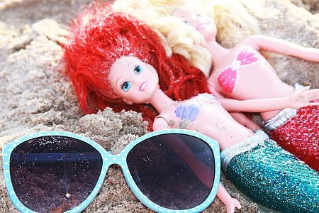 sunglasses and mermaid dolls on sand thumbnail
