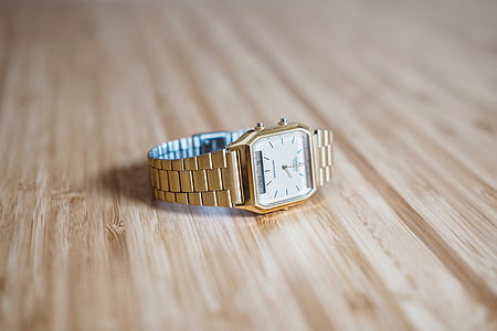square gold-colored analog watch with link band on beige surface thumbnail