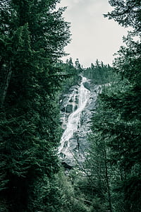 water falls between green leafed trees under white clouds at daytime thumbnail