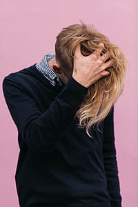 man holding his hair while standing in front of pink wall thumbnail