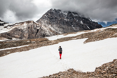 person walking on snow covered ground overlooking grey mountain thumbnail