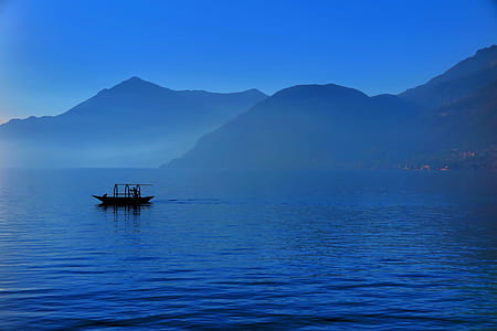 silhouette photo of boat on body of water in front of mountain thumbnail