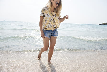 photo of woman wearing brown, gray ,and black floral top and blue short shorts walking in seashore thumbnail