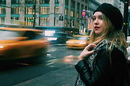 time lapse photography of woman standing on sidewalk fronting road with passing cars thumbnail