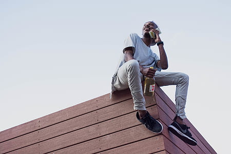 man sitting on ledge holding bottle and talking on smartphone thumbnail