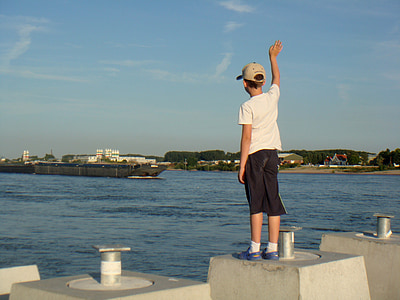 boy standing on concrete block waving on ship at daytime]\ thumbnail