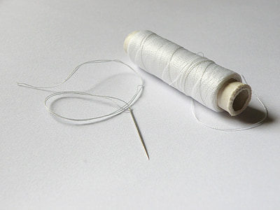 white thread roll beside needle on white surface thumbnail