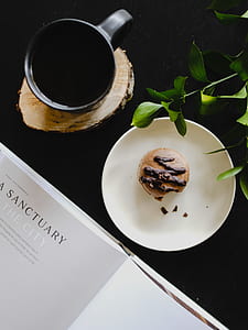 aerial photography of bitten macaron on round white ceramic plate near black ceramic mug filled with coffee on brown wooden coaster thumbnail