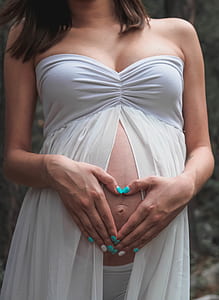 pregnant woman holding tummy doing heart-shape hand gesture wearing tube dress thumbnail